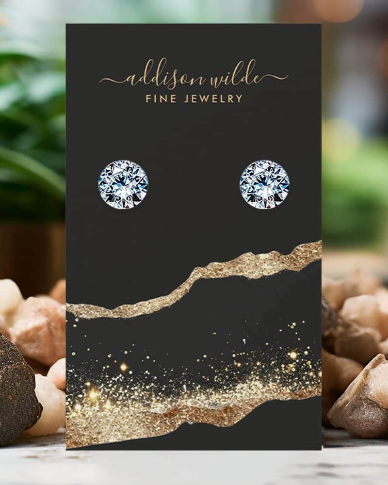 Pair of round diamond stud earrings displayed on a black jewelry card.