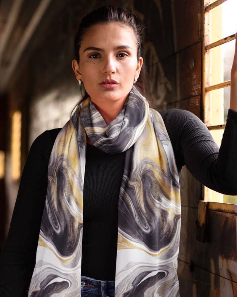 Woman wearing a long, abstract marble patterned scarf in gold, grey, and black.