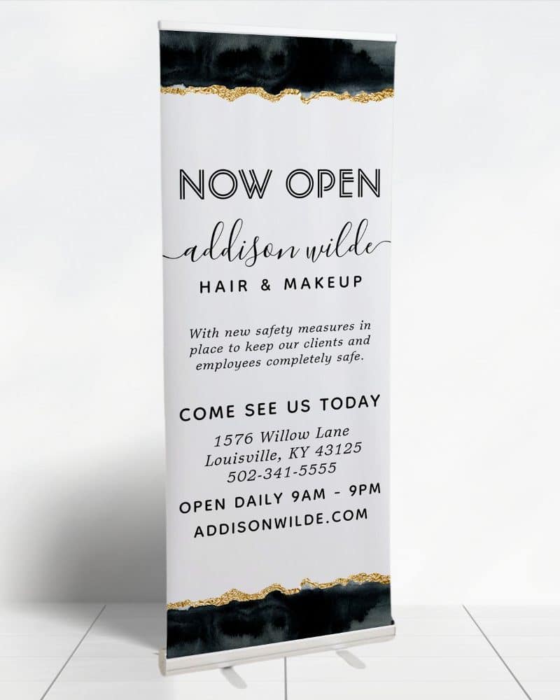 A retractable banner announcing the grand opening of Addison Wilde Hair & Makeup salon. The banner includes the salon's address and hours.
