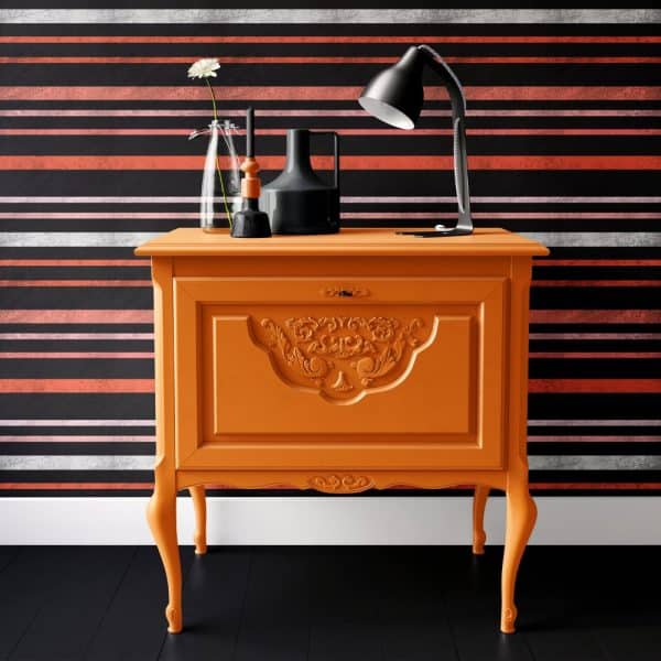 Orange Painted Cabinet With Ornate Detailing, Holding A Lamp And Decorative Objects.