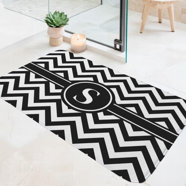 Black And White Chevron Patterned Bath Mat With A Black Circle And The Letter S In The Center.