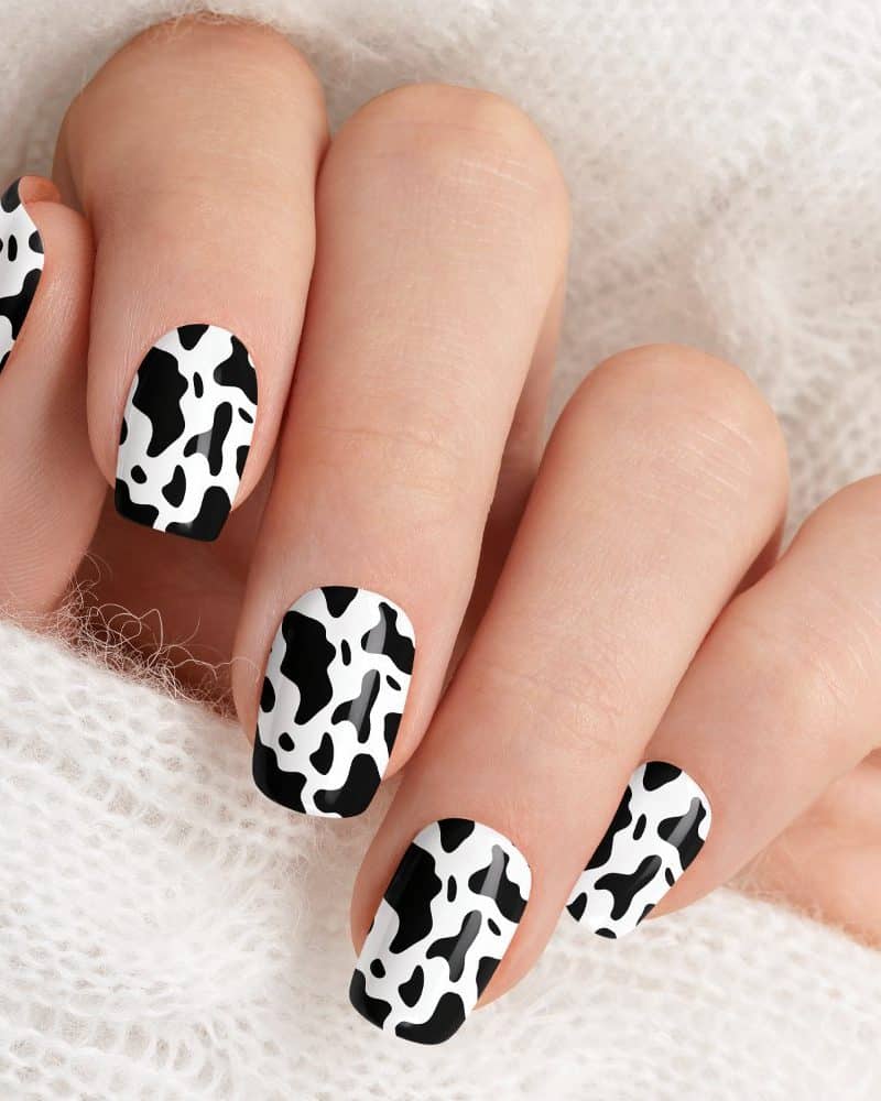 Close-up of a hand with nails painted in a cow print design.