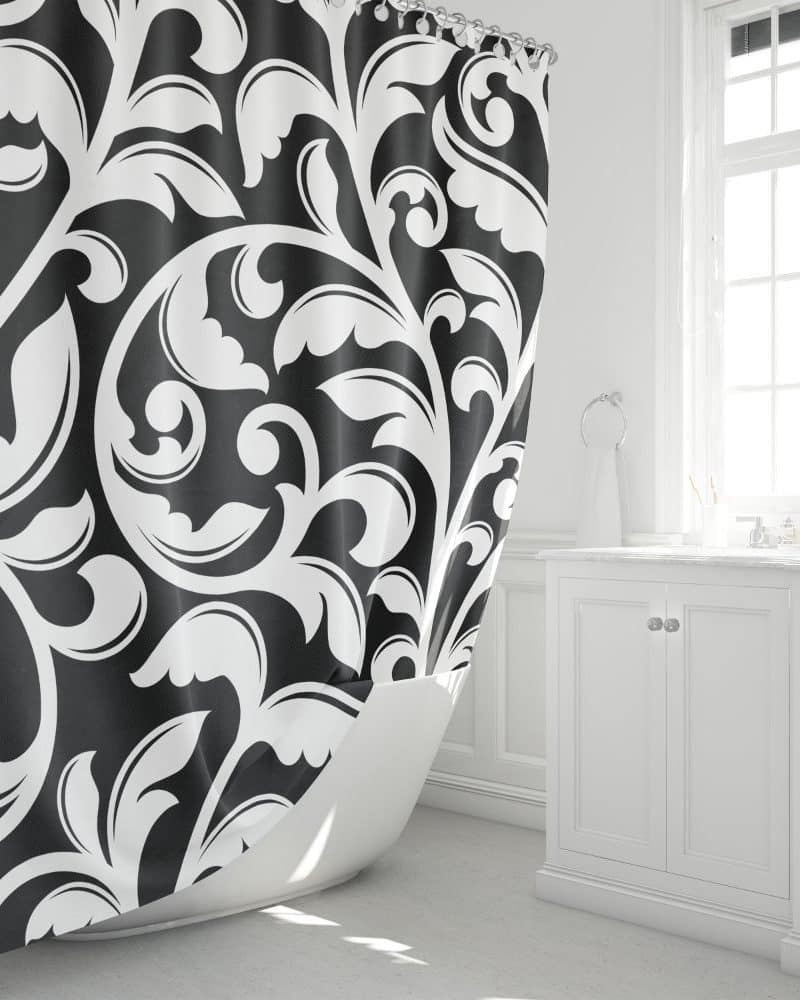 Black and white damask shower curtain partially draped over a white bathtub.