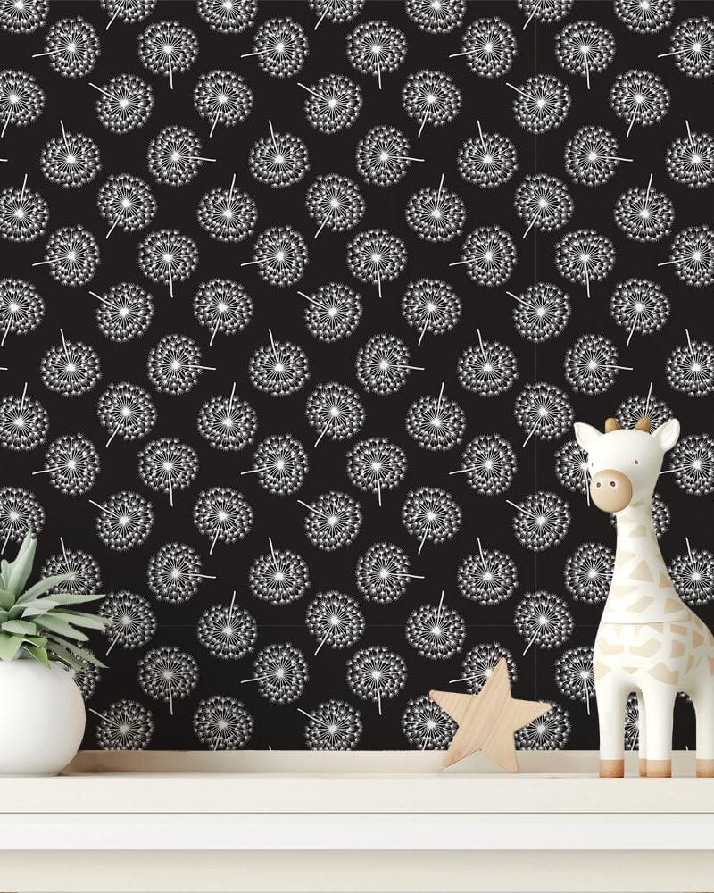 A white giraffe toy and small potted plant sit on a shelf in front of a black wall covered in a dandelion seedhead pattern.