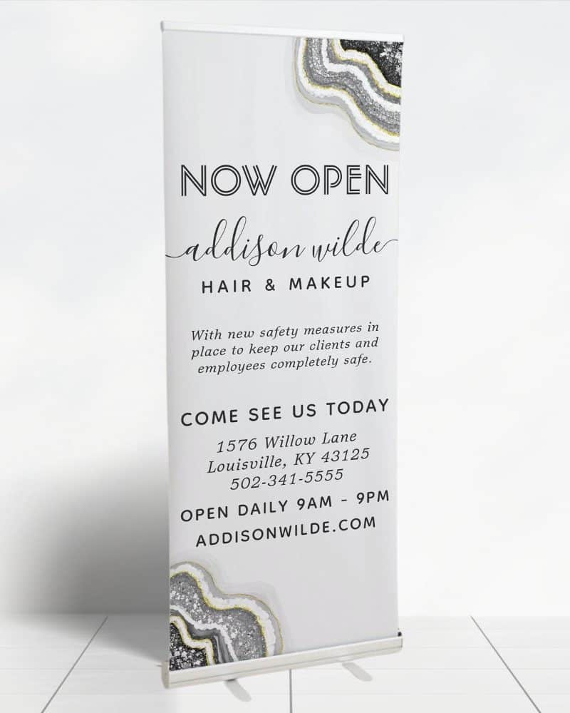A retractable banner announcing the grand opening of Addison Wilde Hair & Makeup salon, including the address and hours.