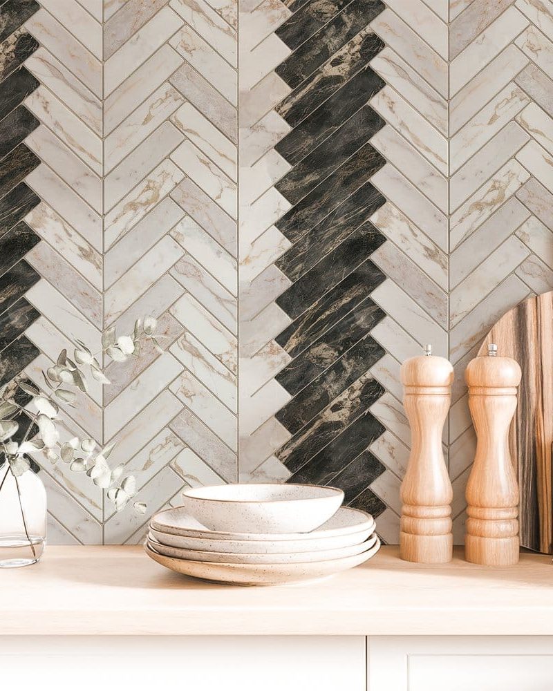 A kitchen counter with stacked dishes, salt and pepper shakers, and a cutting board in front of a herringbone patterned backsplash in shades of beige and dark brown.
