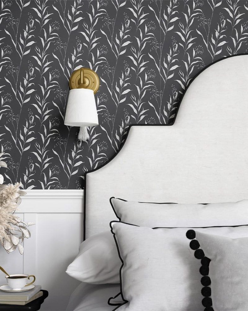 Dark gray wallpaper with a repeating pattern of white stylized leaves and branches, partially visible behind a white headboard.