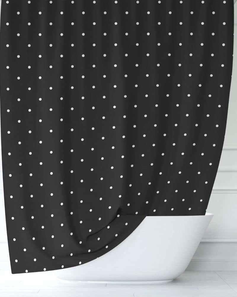 Black shower curtain with small white polka dots partially draped over a white bathtub.