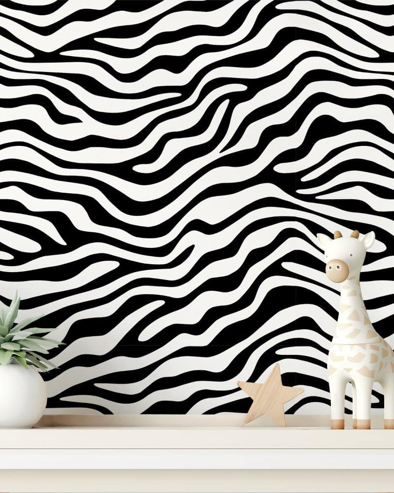 A white giraffe toy and small potted plant sit on a shelf in front of a black and white zebra striped wall.