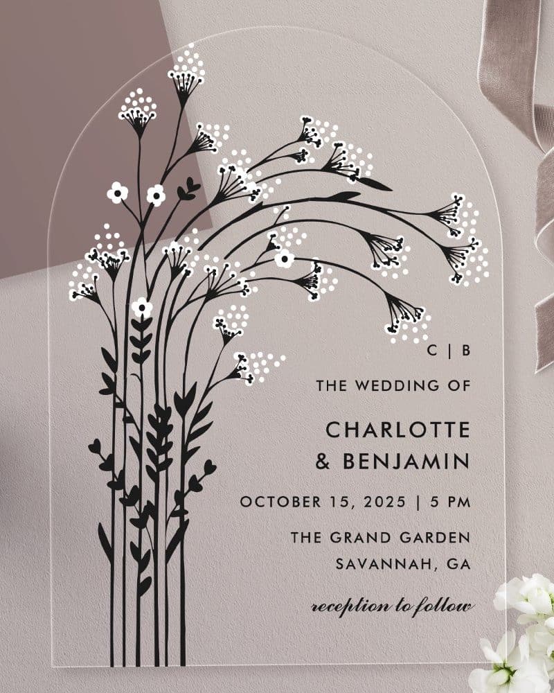 Arch-shaped clear acrylic wedding invitation with black floral design and white details, featuring the couple's names and wedding details.