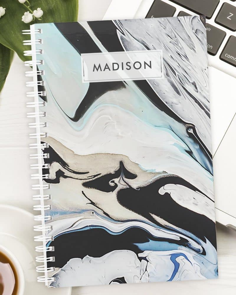 Spiral-bound notebook with an abstract marble design in black, white, and blue; the name Madison is printed on the cover.