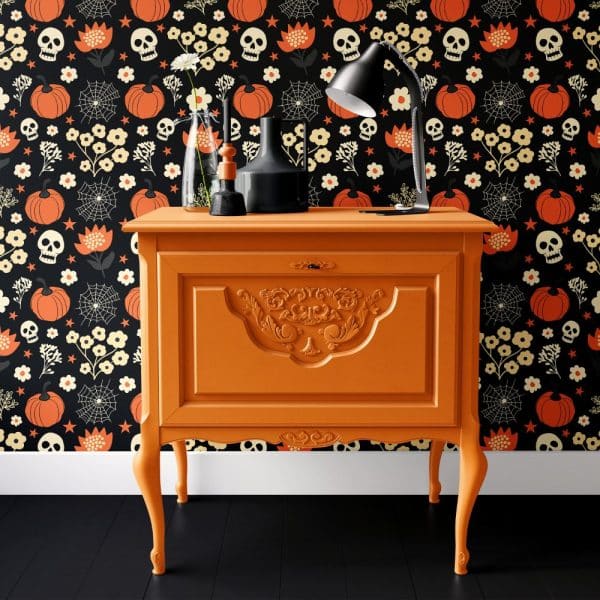 An Orange Painted Wooden Cabinet With Ornate Detailing Sits Against A Halloween-Themed Wall.