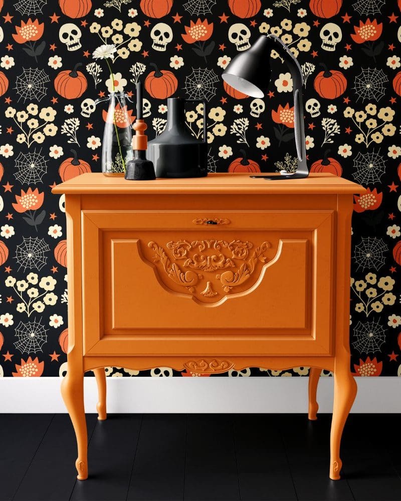 An orange painted wooden cabinet with ornate detailing sits against a Halloween-themed wall.