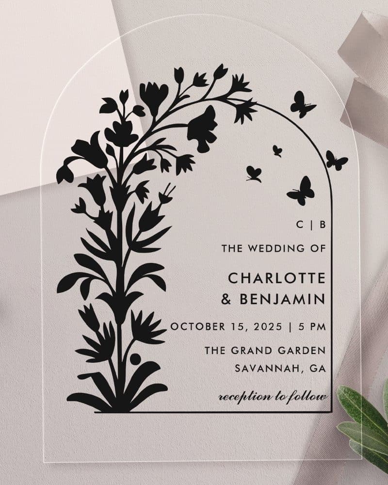 Arch-shaped clear acrylic wedding invitation with black floral illustration and wedding details.