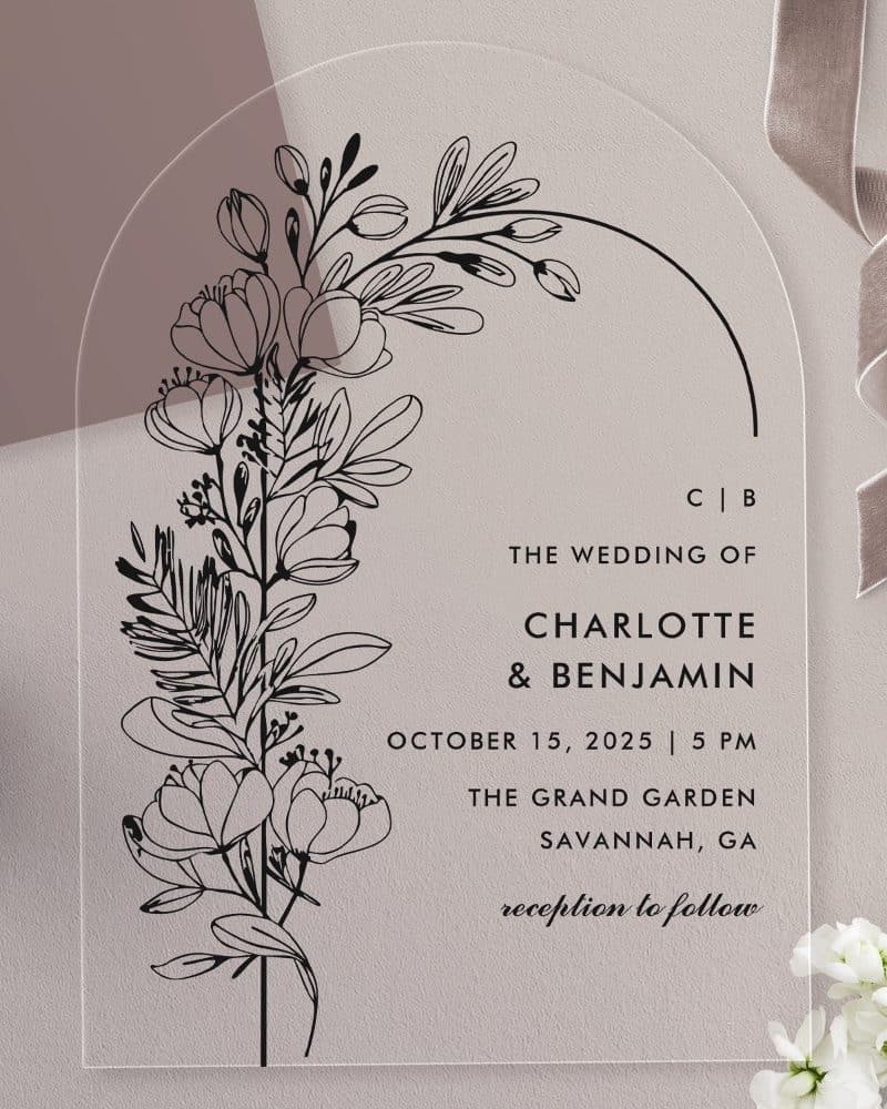 Arch-shaped clear acrylic wedding invitation with black line floral design and wedding details.