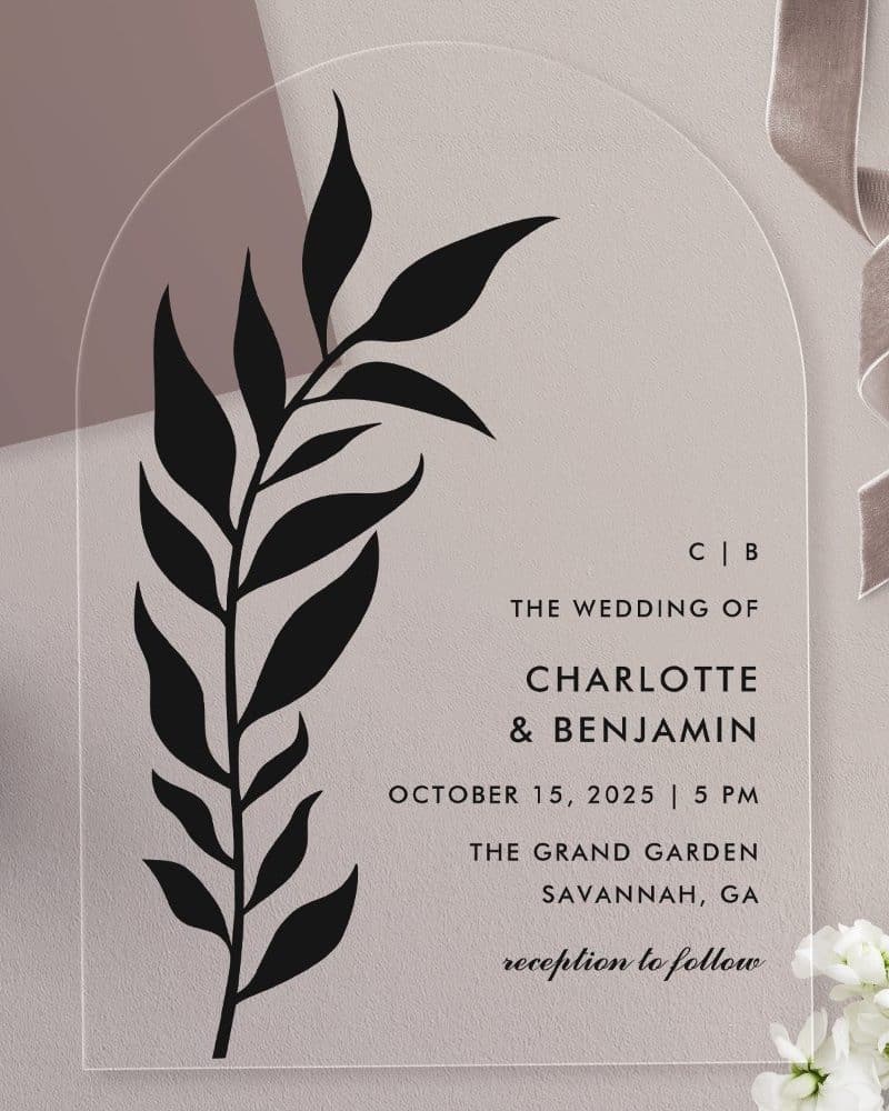 Arch-shaped clear acrylic wedding invitation with a black floral design and the names Charlotte and Benjamin.