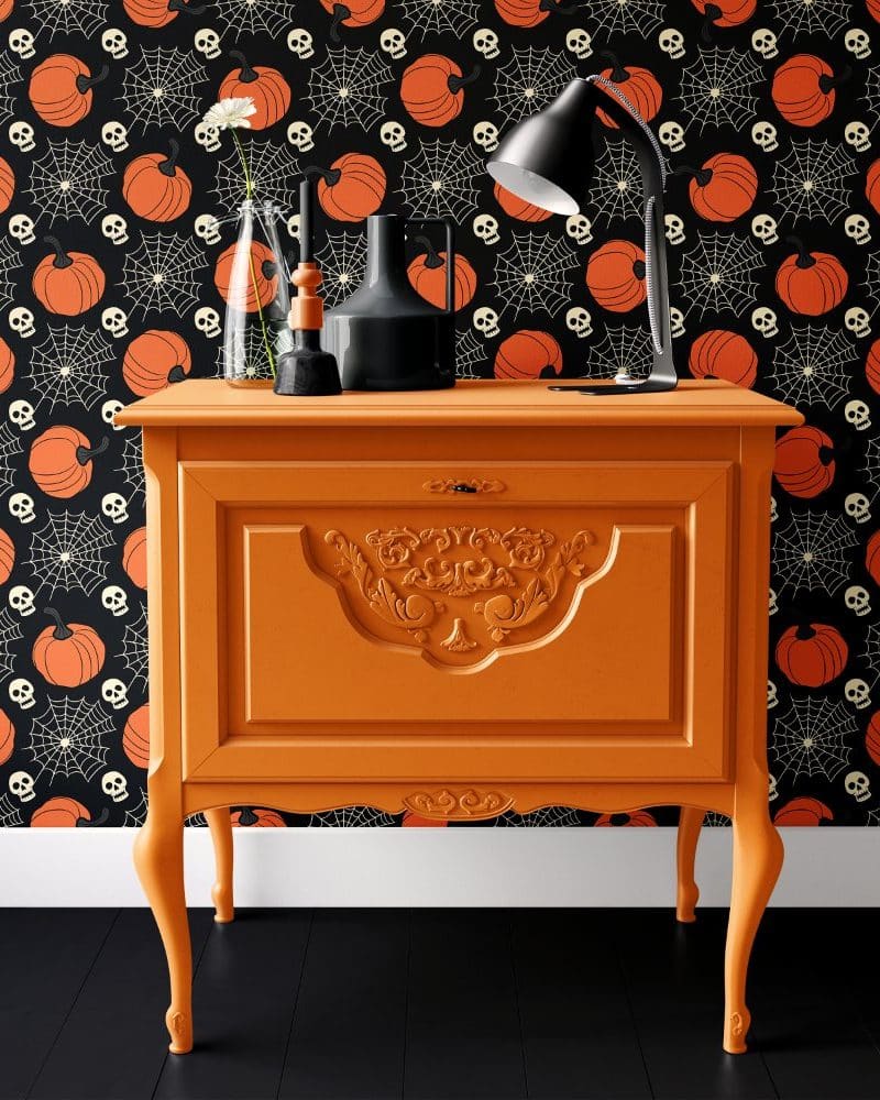 Orange dresser with ornate details against a Halloween-themed wallpaper.