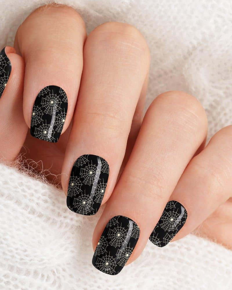 Closeup of a hand with black fingernails decorated with a pattern of white spiderwebs.