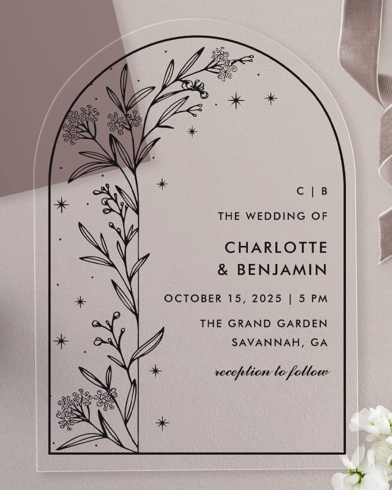 Arch-shaped clear acrylic wedding invitation with black floral illustration and wedding details.