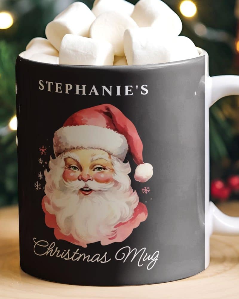 A black Christmas mug with a vintage Santa illustration, personalized with the name Stephanie's, filled with marshmallows.