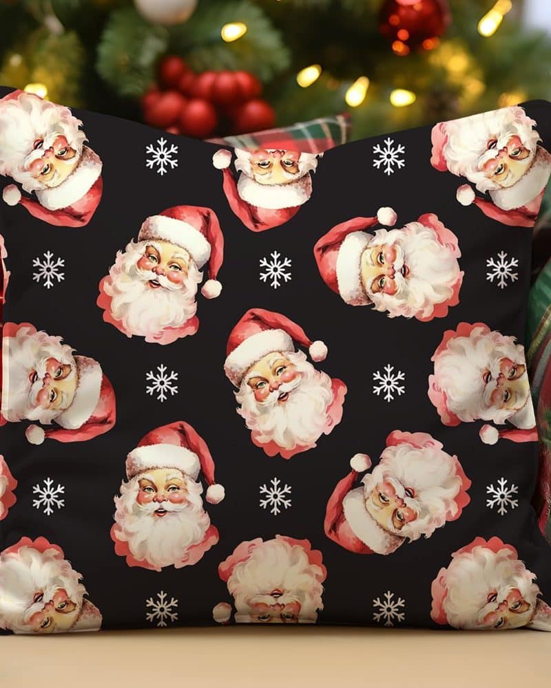 Black throw pillow with a repeating pattern of Santa Claus faces and snowflakes.
