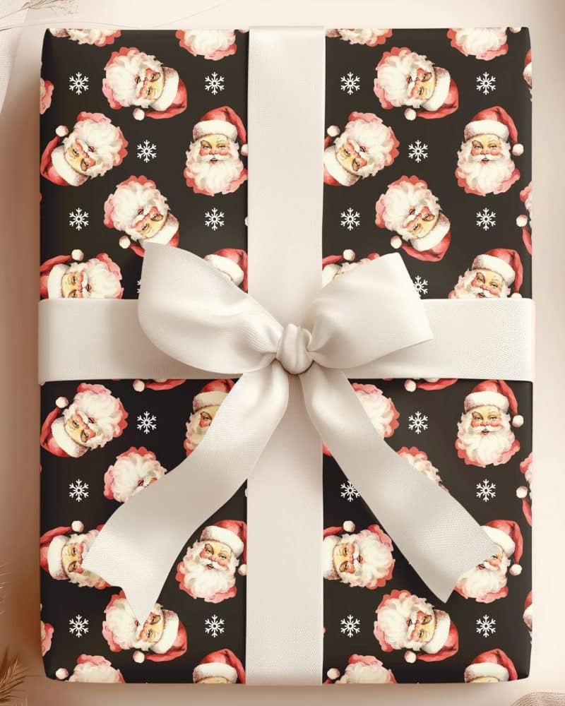 A Christmas gift wrapped in dark paper featuring a repeating pattern of Santa Claus faces and snowflakes, tied with a cream-colored ribbon.
