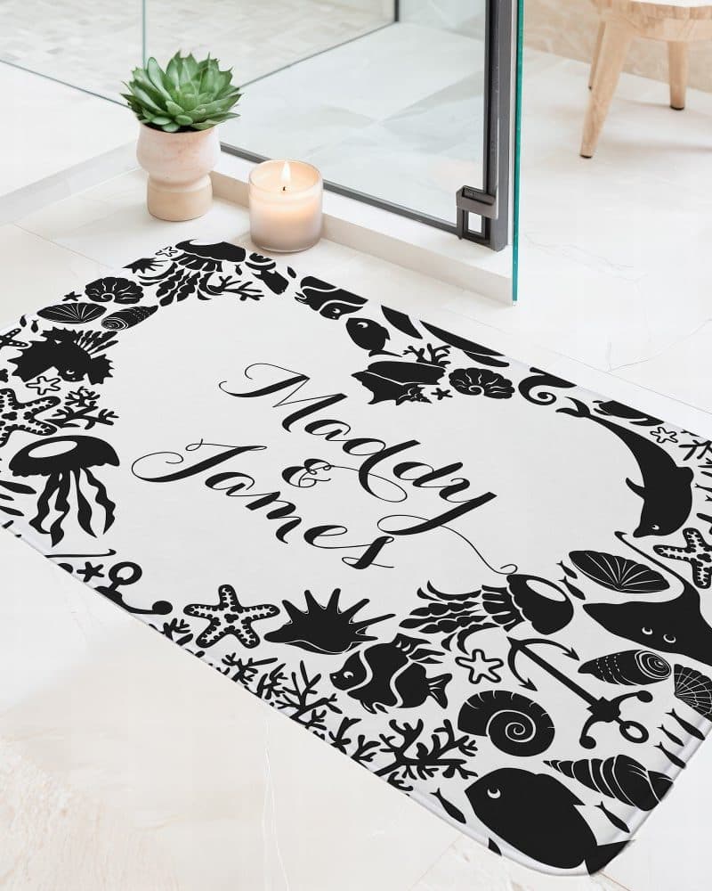 A white bath mat with black silhouettes of sea creatures and the names Madaly and James.