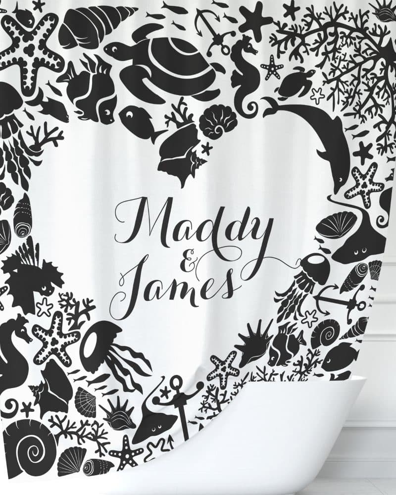A white shower curtain with a black heart-shaped border of sea creatures and the names Maddy & James in the center.