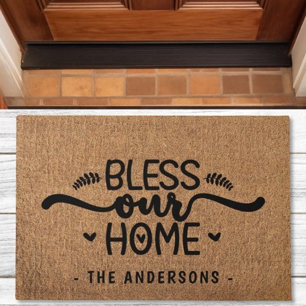 Tan Doormat With Black Lettering That Says Bless Our Home, With The Family Name The Andersons Below.