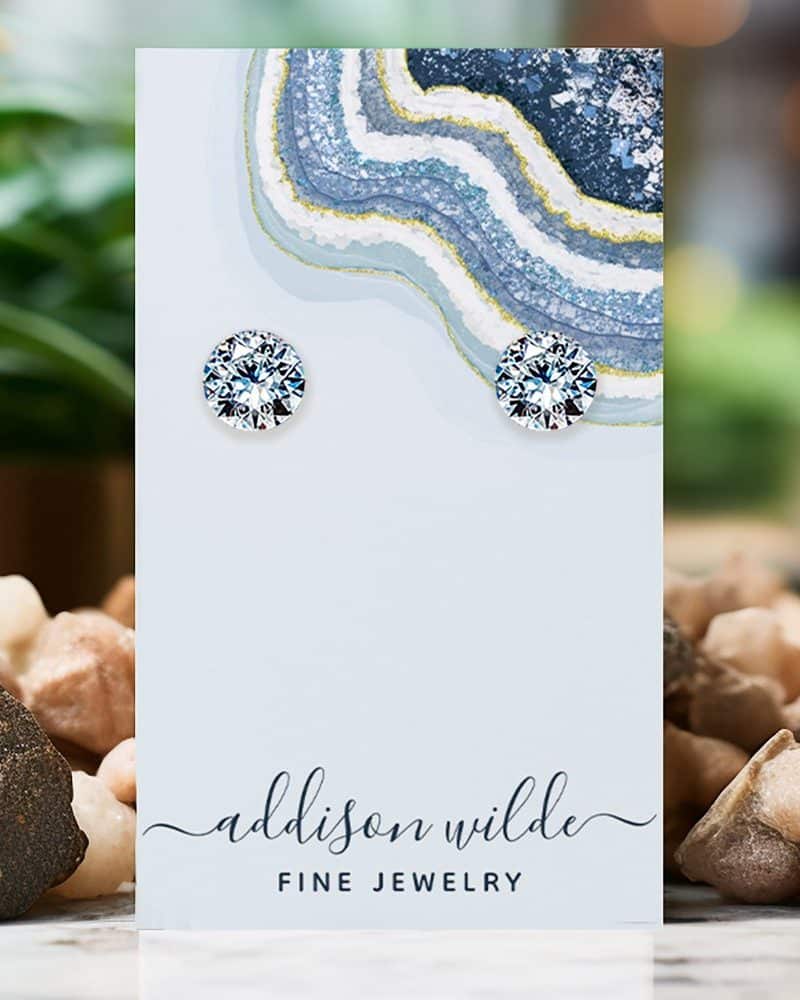 Pair of round, clear gemstone stud earrings displayed on a light blue jewelry card.