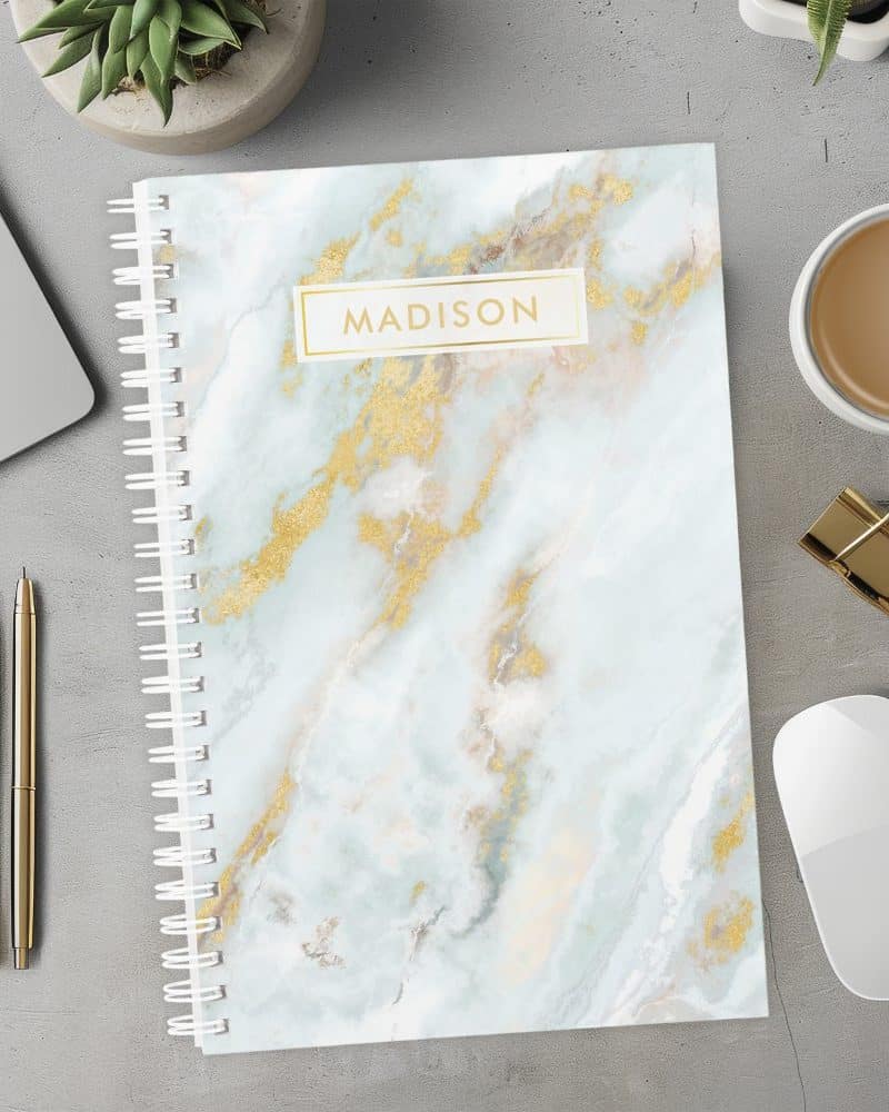 Spiral-bound notebook with a light blue marble cover and gold accents; the name Madison is printed on the cover.