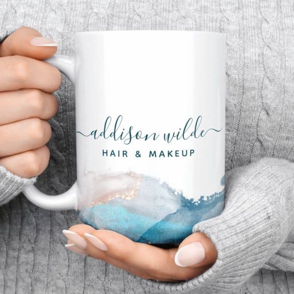 Hands Holding A White Coffee Mug With The Name Addison Wilde Hair &Amp; Makeup And An Abstract Teal Design.