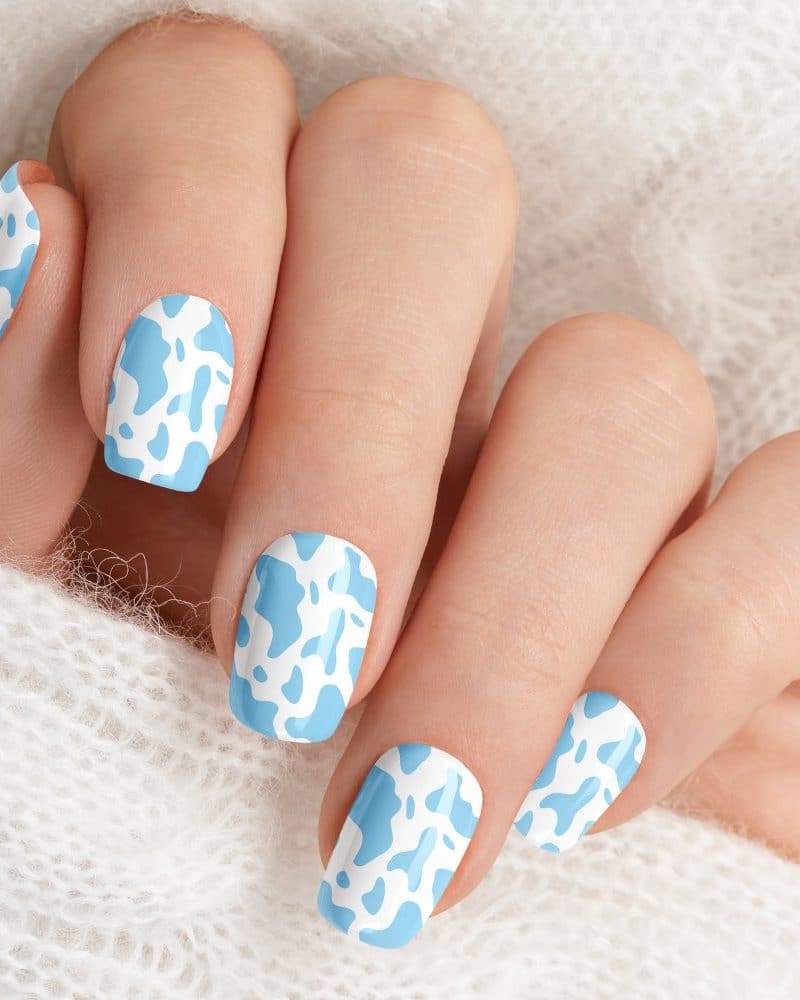 Close-up of a hand with light blue cow print nail polish.