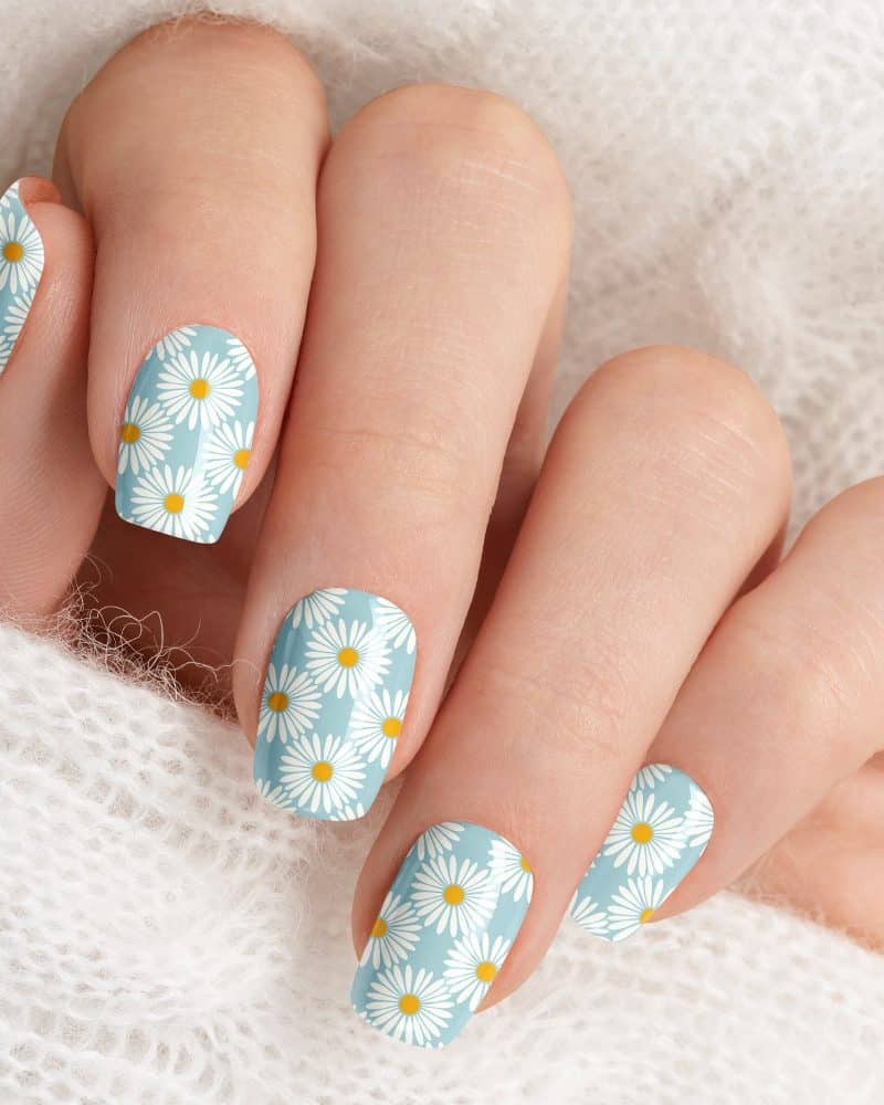 Closeup of a hand with light blue nails decorated with a daisy pattern.