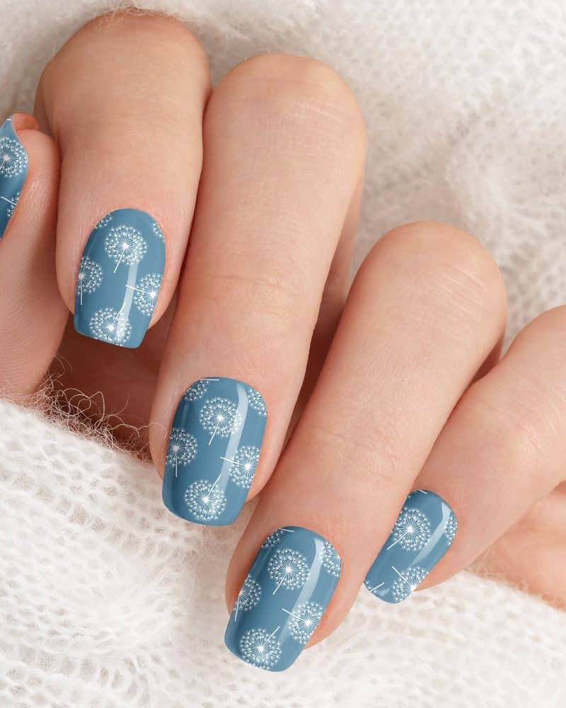 Woman's hand with blue nails decorated with a white dandelion pattern.