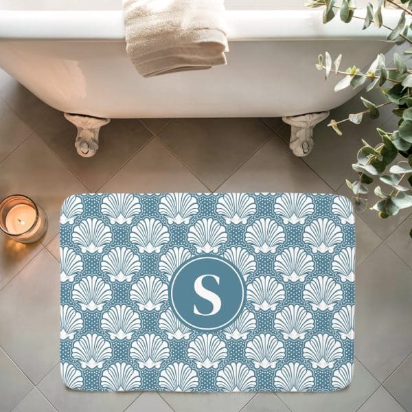 Blue Bath Mat With A White Seashell Pattern And A Teal Monogrammed S In The Center.