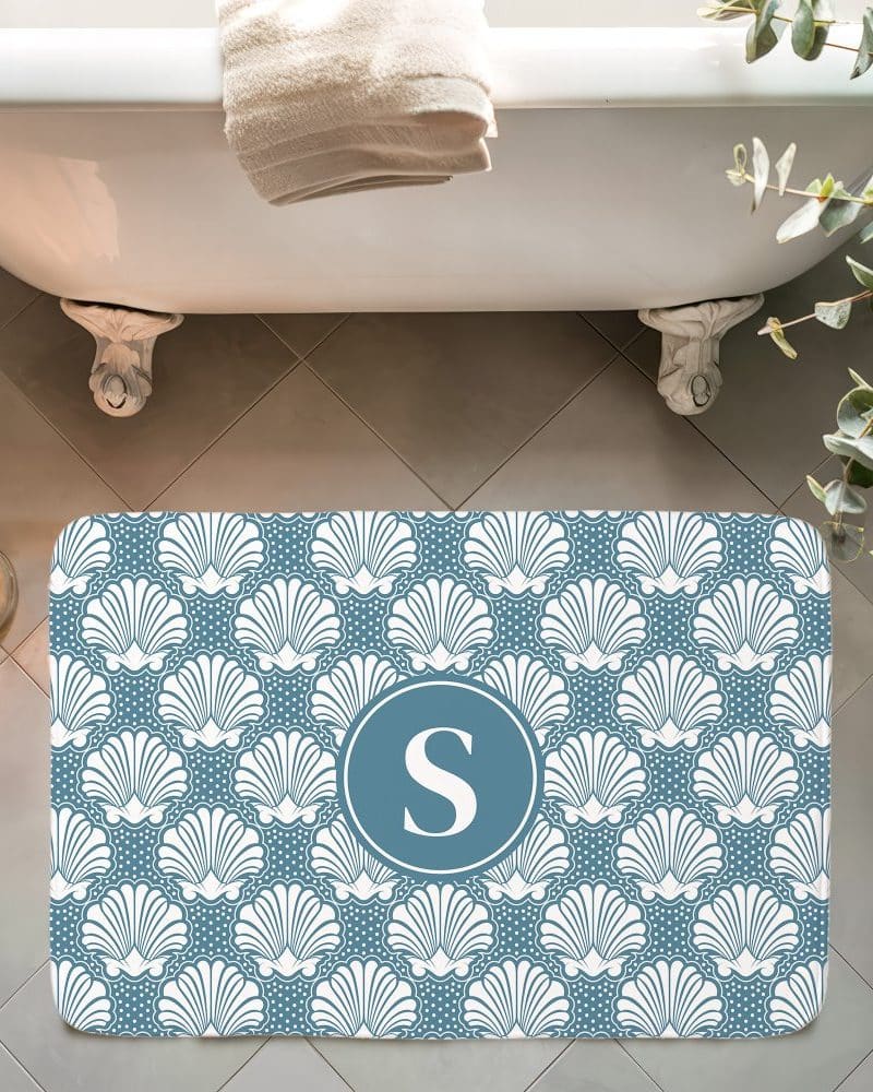 Blue bath mat with a white seashell pattern and a teal monogrammed S in the center.