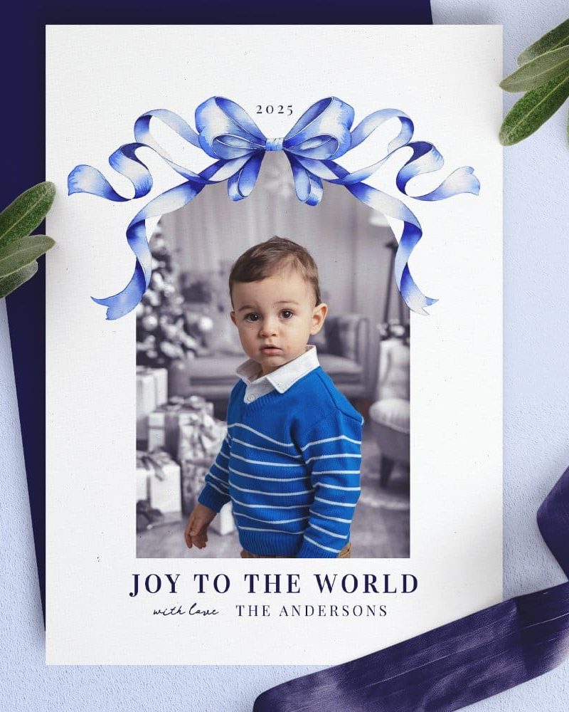Christmas card featuring a toddler boy in a blue striped sweater, framed by a blue watercolor bow.
