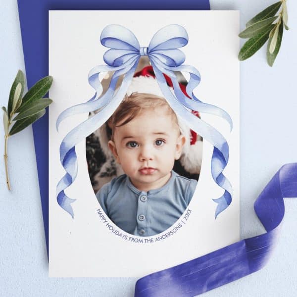 Holiday Card Featuring A Baby'S Photo Framed By A Large Blue Watercolor Bow.