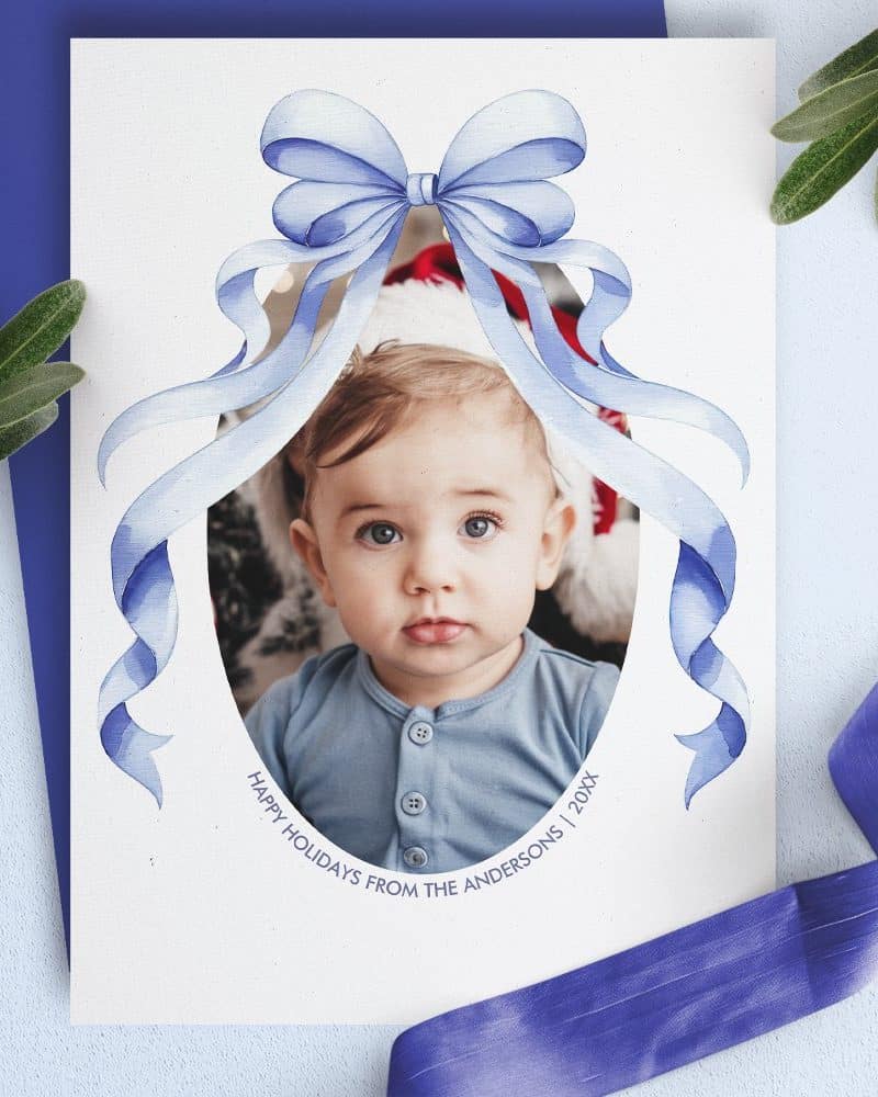 Holiday card featuring a baby's photo framed by a large blue watercolor bow.