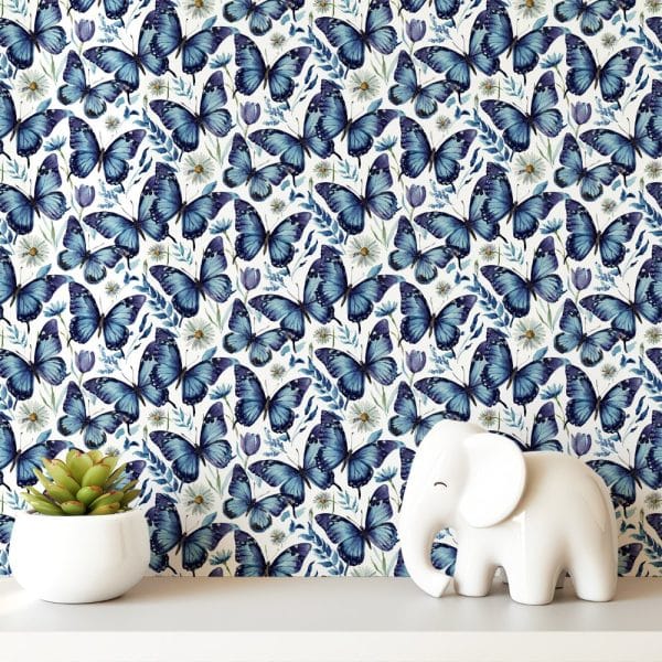 A White Shelf Displays A White Elephant Figurine In Front Of Wallpaper Featuring A Repeating Pattern Of Blue Butterflies And Small Flowers.