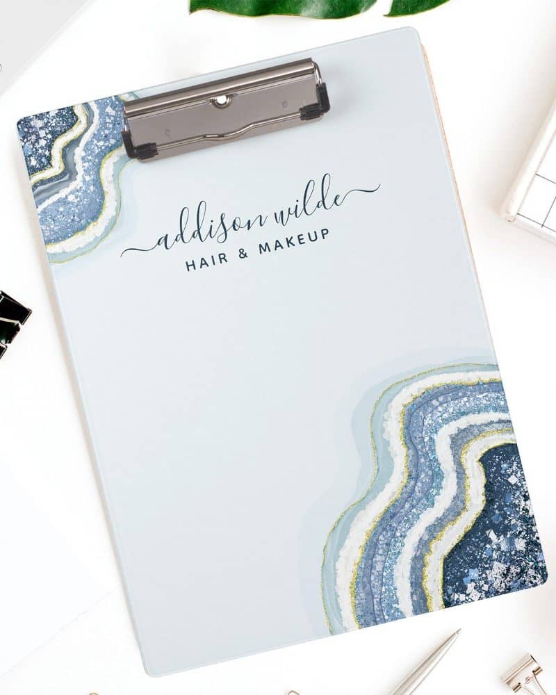 A light blue clipboard with a blue and gold agate design and Addison Wilde Hair & Makeup text.