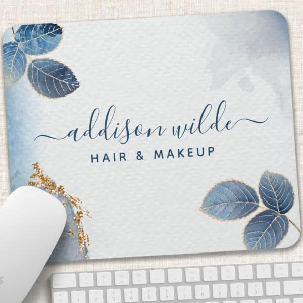A Light Blue Mousepad With The Name Addison Wilde Hair &Amp; Makeup In Dark Blue Script Lettering, Accented With Gold And Blue Watercolor Leaves.
