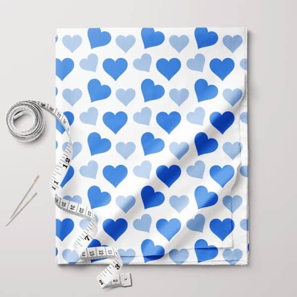 White Fabric With A Repeating Pattern Of Light And Dark Blue Hearts, Accompanied By A Measuring Tape And Sewing Needles.