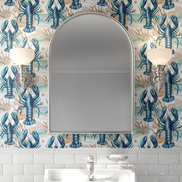Bathroom Mirror With Arched Top, Flanked By Wall-Mounted Lights, All Set Against A Wall Covered In Wallpaper Featuring A Repeating Pattern Of Blue Lobsters And Seashells.