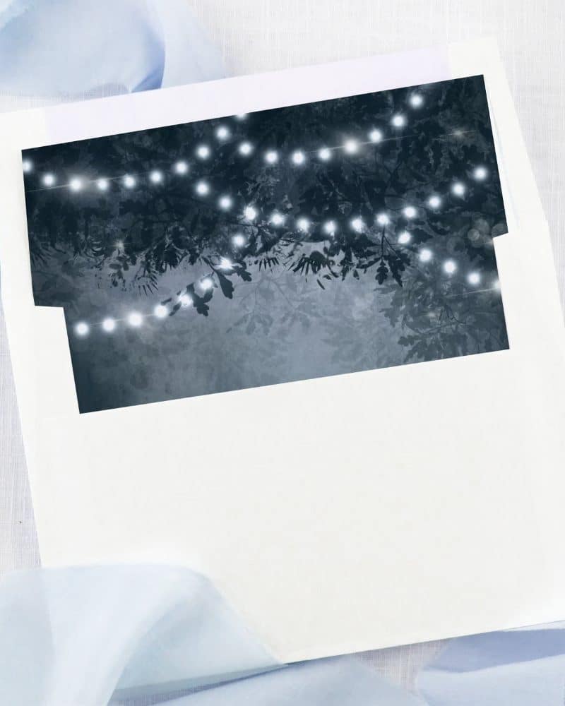 White envelope with a dark blue liner featuring string lights in trees.
