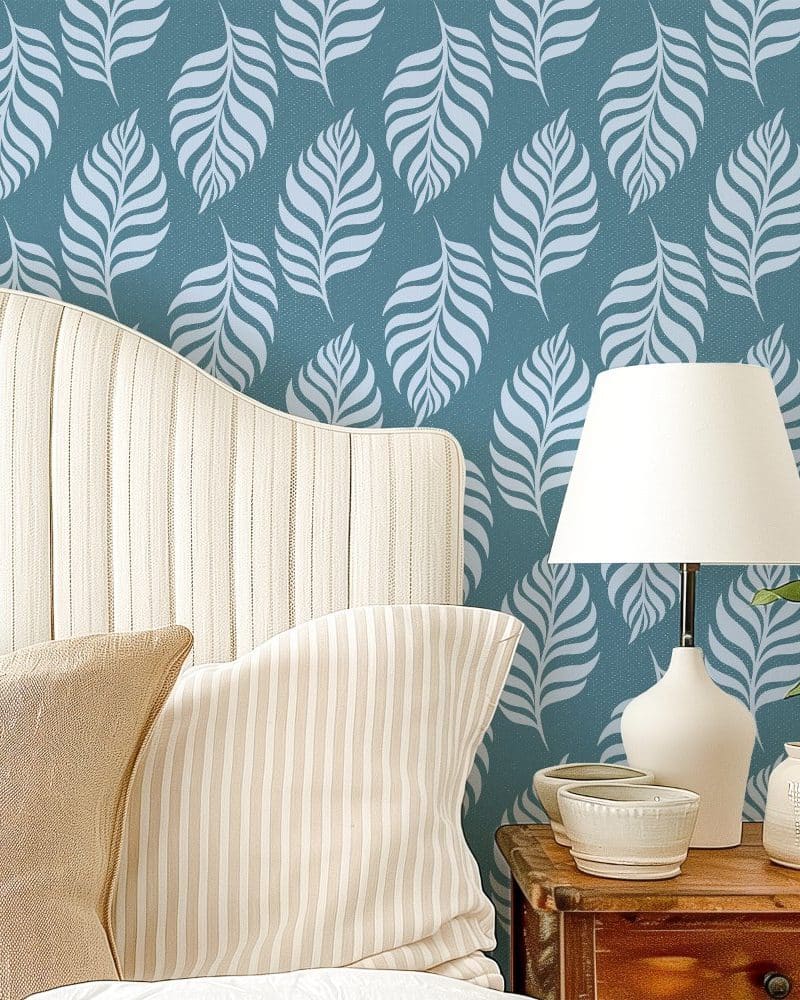 A bed with a curved headboard and striped pillows is positioned against a teal wall with a repeating leaf pattern.