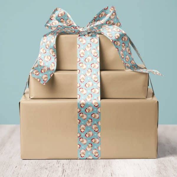 A Stack Of Three Brown Gift Boxes Tied With A Blue Ribbon Featuring A Repeating Santa Claus Pattern.