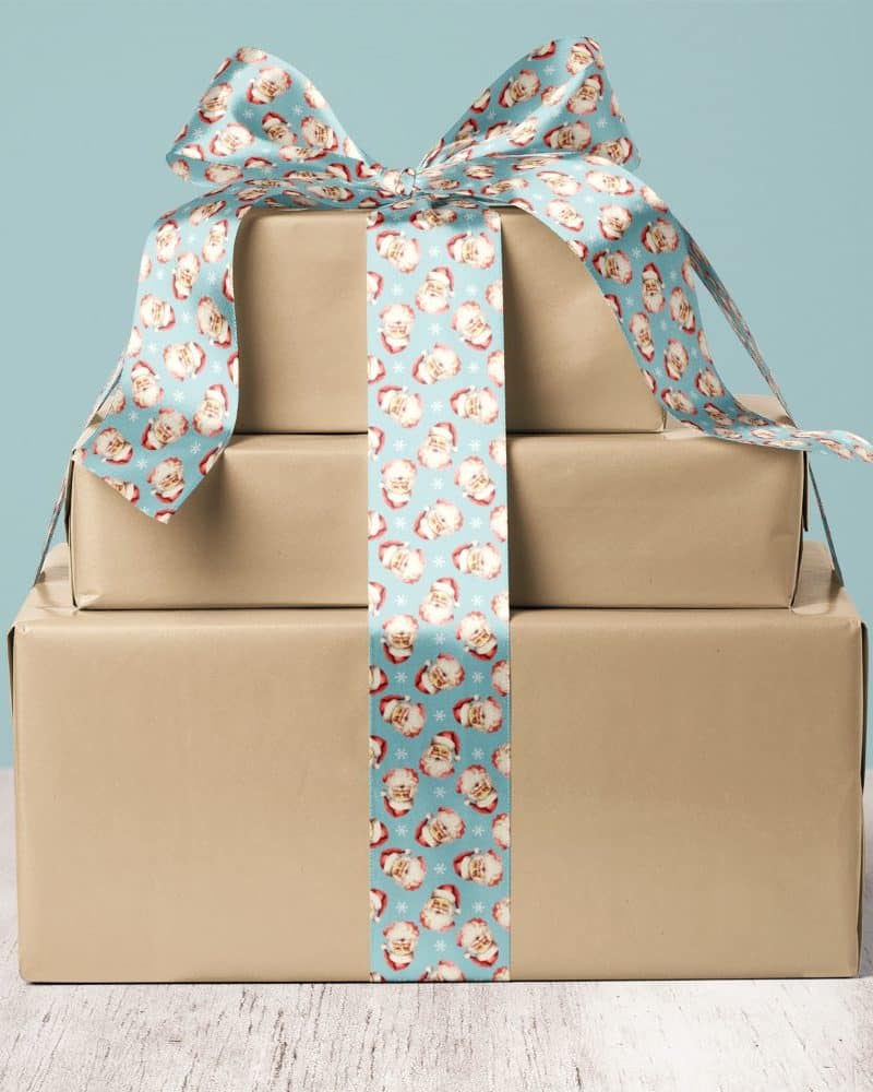 A stack of three brown gift boxes tied with a blue ribbon featuring a repeating Santa Claus pattern.
