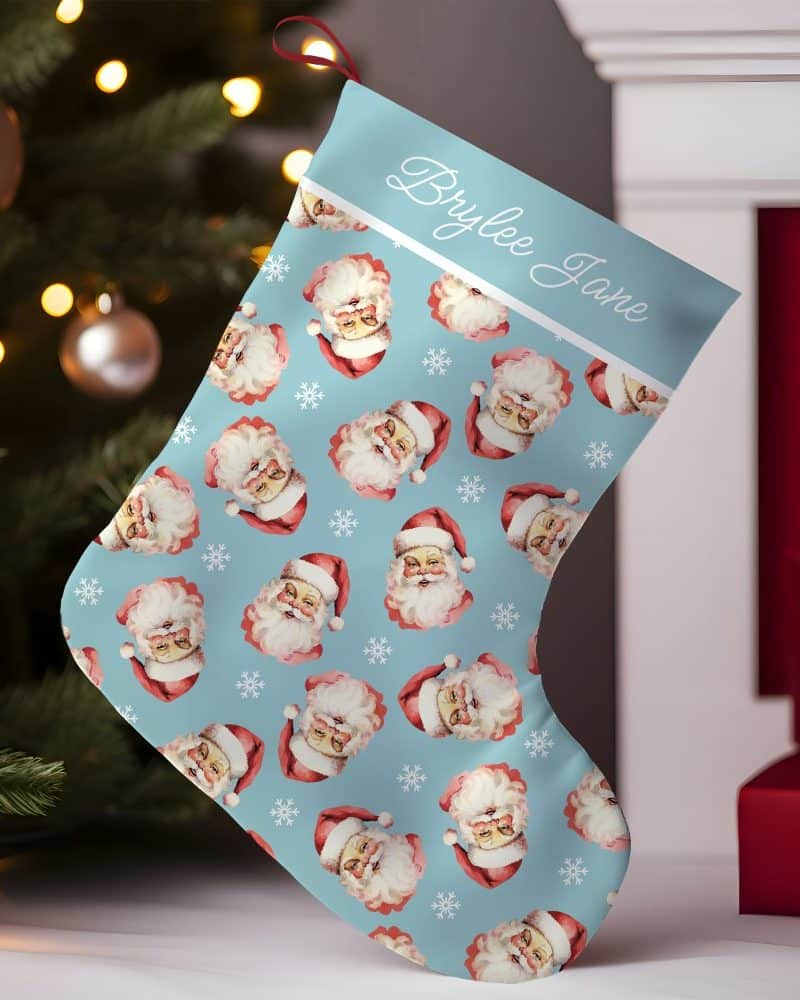 Personalized Christmas stocking with a light blue background and a repeating pattern of Santa Claus faces. The stocking is labeled Brylee Jane.